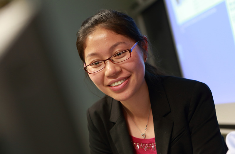 Smiling woman with glasses in a business suit at a Health Services Administration lecture.